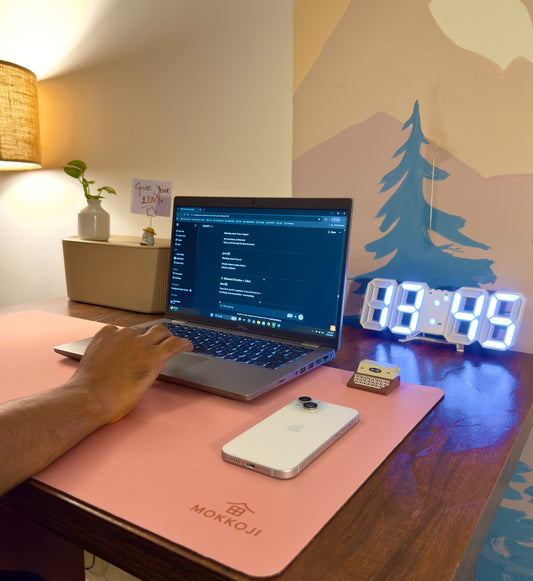 A person using a laptop on a desk with a pink Desk mat, a digital clock, and a cable management box. A clutter-free experience