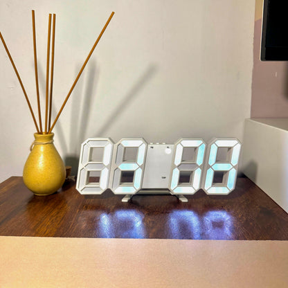 Digital clock on a wooden surface with a vase and sticks in the background