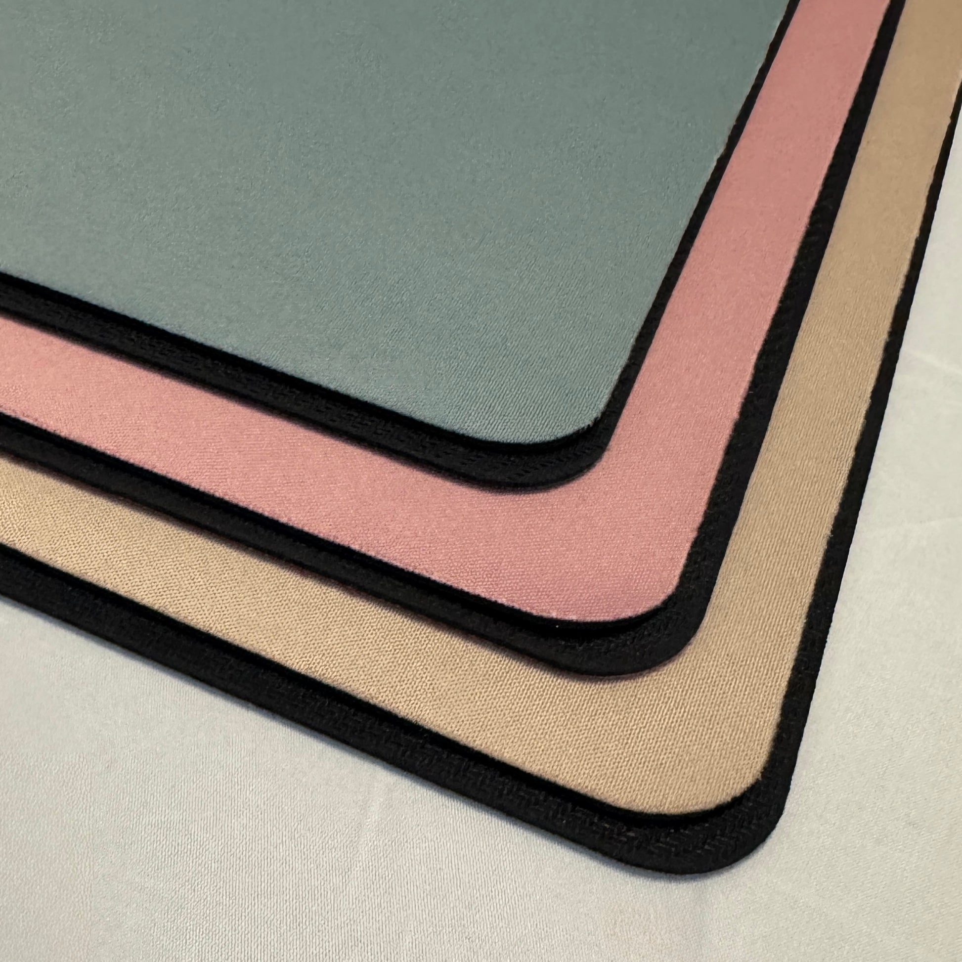Close-up of 3 rectangular desk mats in green, pink, beige to show their texture