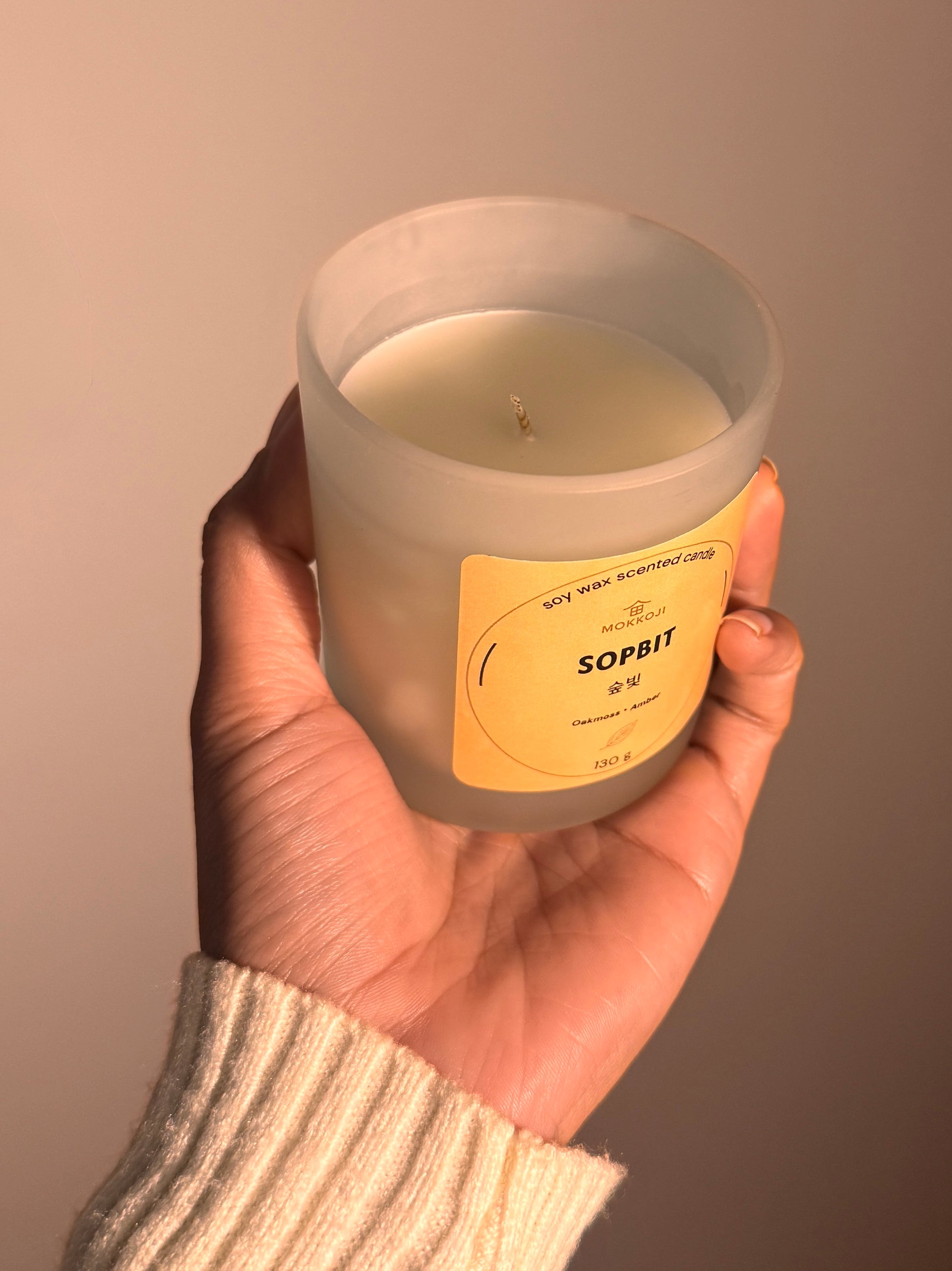 Hand holding a candle labeled 'Sopbit' against a plain background